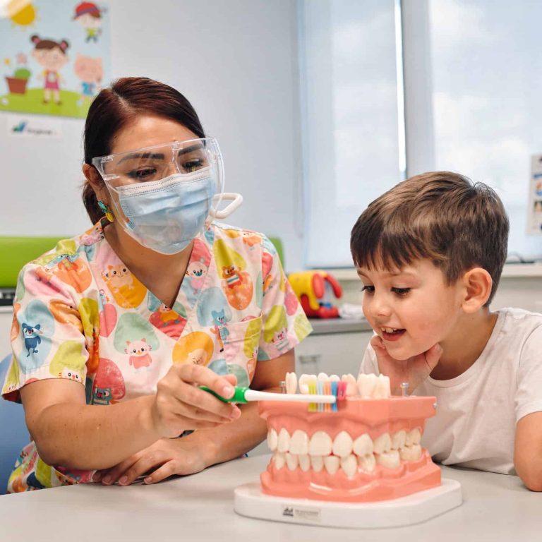 Pediatric dentist showing a young boy a dental model to promote good oral hygiene.
